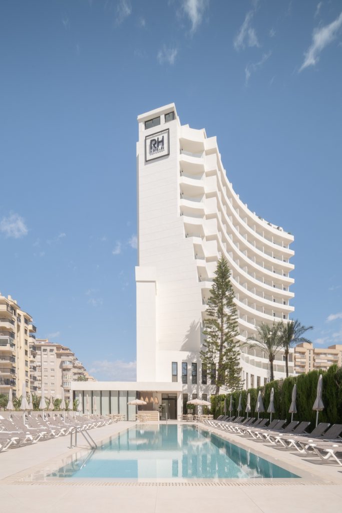 Vista exterior diurna de la torre del Hotel RH Arena Gandía con logotipo RH Hoteles y cielo azul