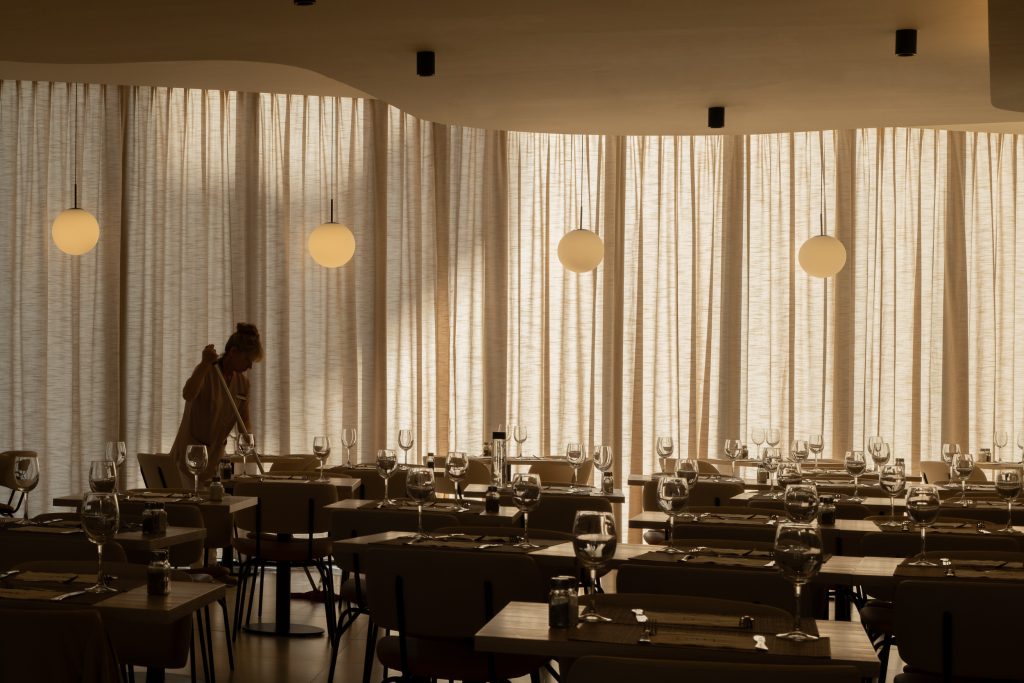 Restaurante del Hotel RH Arena Gandía con mesas preparadas, cortinas de lino y lámparas esféricas