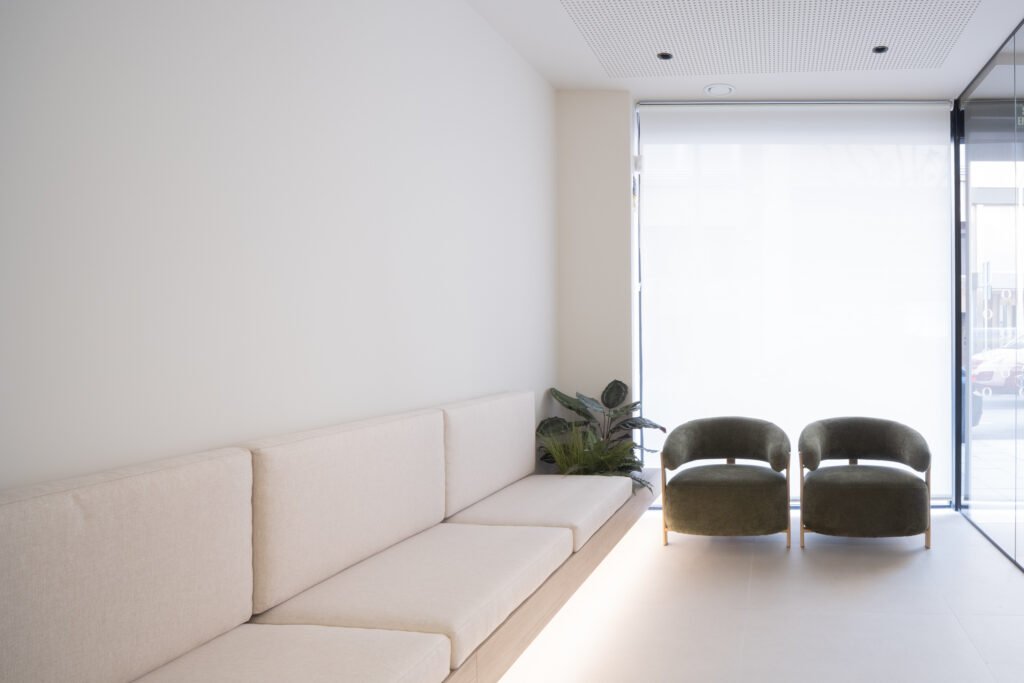 Sala de espera de la clínica dental Odentia con sofá beige, sillones verdes y gran ventanal con luz natural