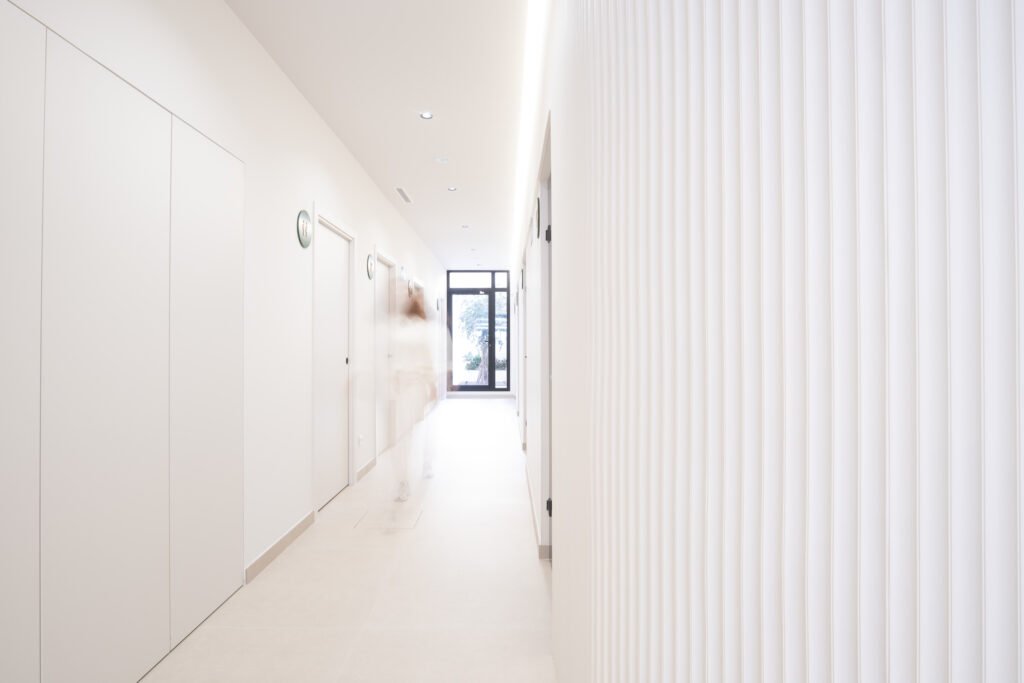 Pasillo blanco y luminoso de la clínica dental Odentia con paneles de lamas verticales y luz natural al fondo