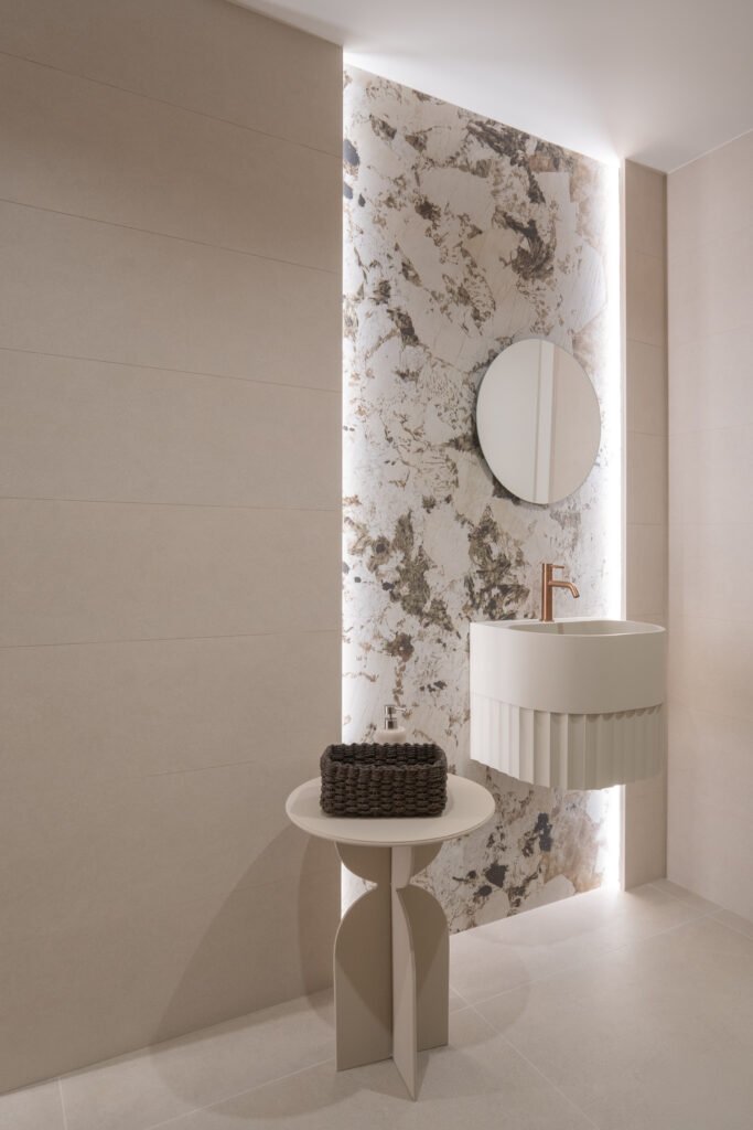 Baño de diseño de la clínica dental Odentia con lavabo redondo, pared con revestimiento de cerámica XTone retroiluminada y espejo circular