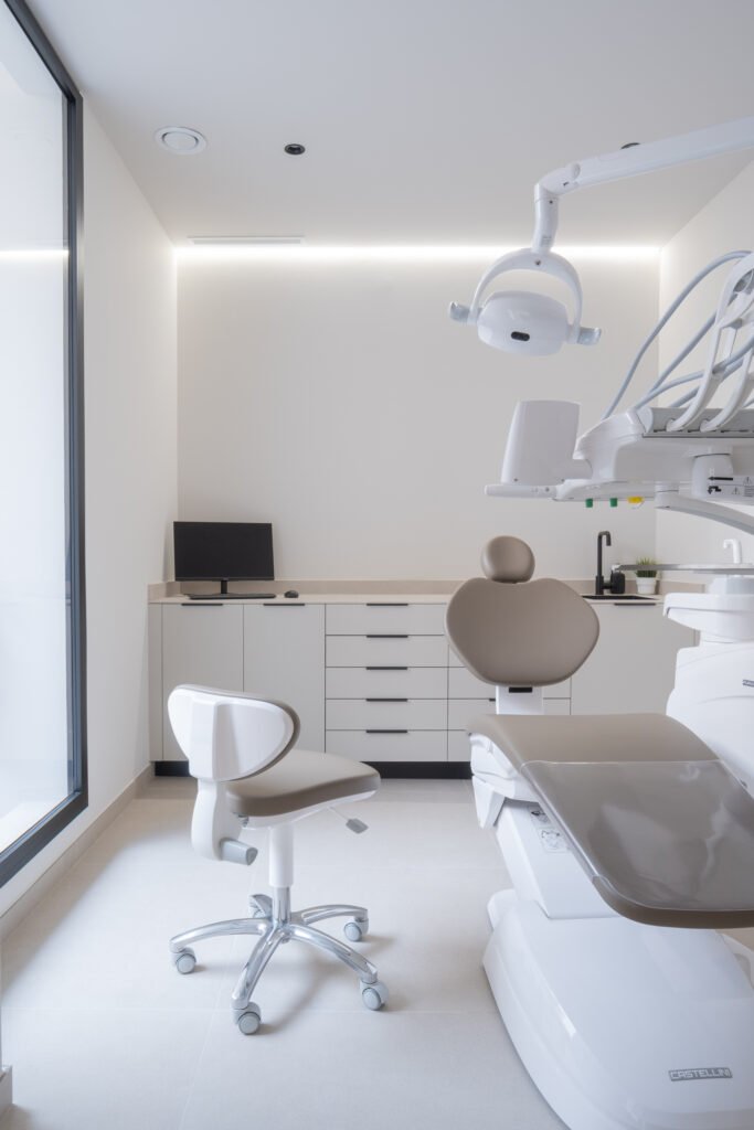 Gabinete dental moderno con sillón beige, lámpara cenital y mobiliario blanco en clínica Odentia
