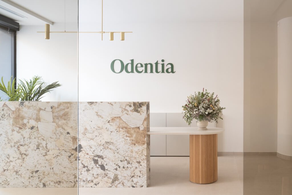Recepción de la clínica dental Odentia con mostrador de cerámica en gran formato, rótulo corporativo verde y ramo de flores