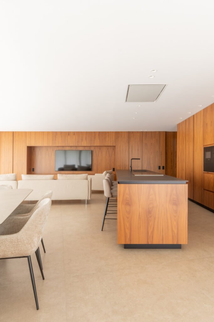 Salón con panel de madera y televisor integrado junto a la cocina — Casa en el Mediterráneo, Fran Esbrí Studio, Castellón | Jesús Castelló